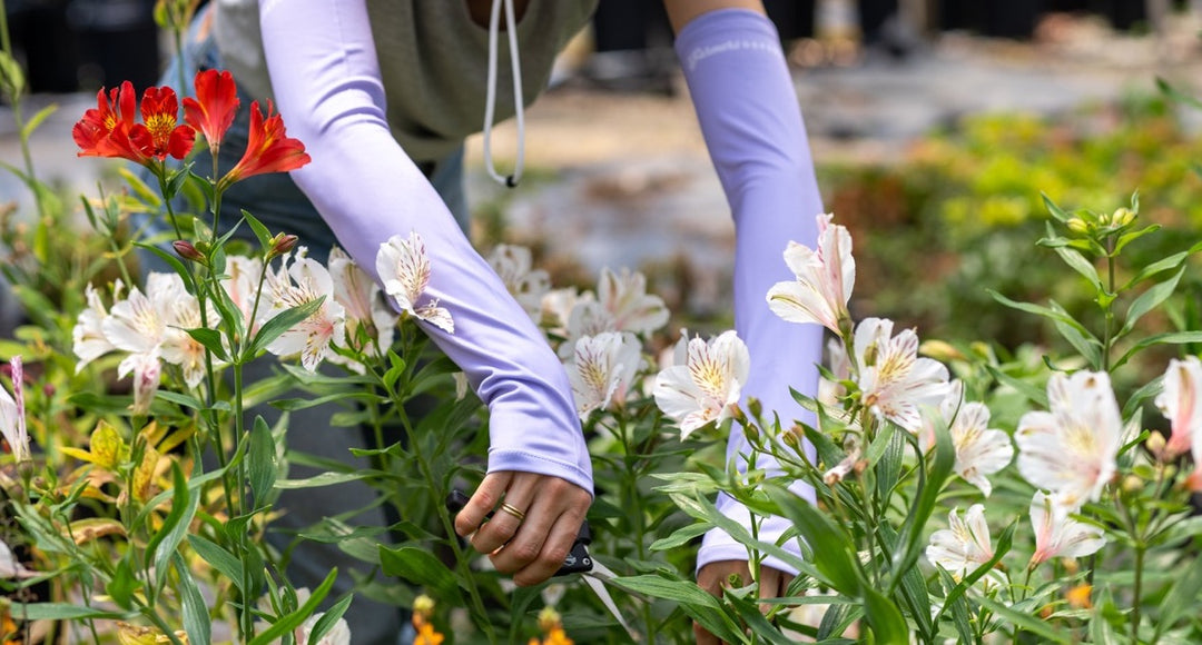 A woman bending over a flower box to trim some leaves.